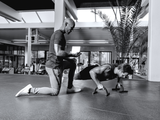 personal trainer Dario Di Lorenzo die met een timer in kniezit voor een klant zit die een push up uitvoert